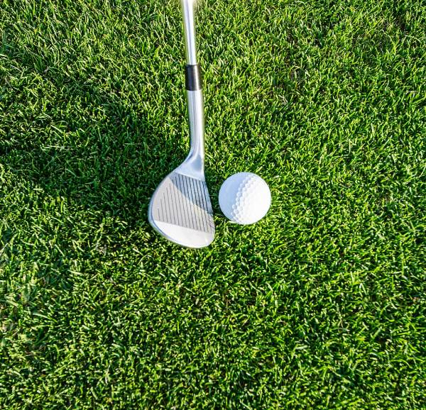 Golf wedge and ball on green grass